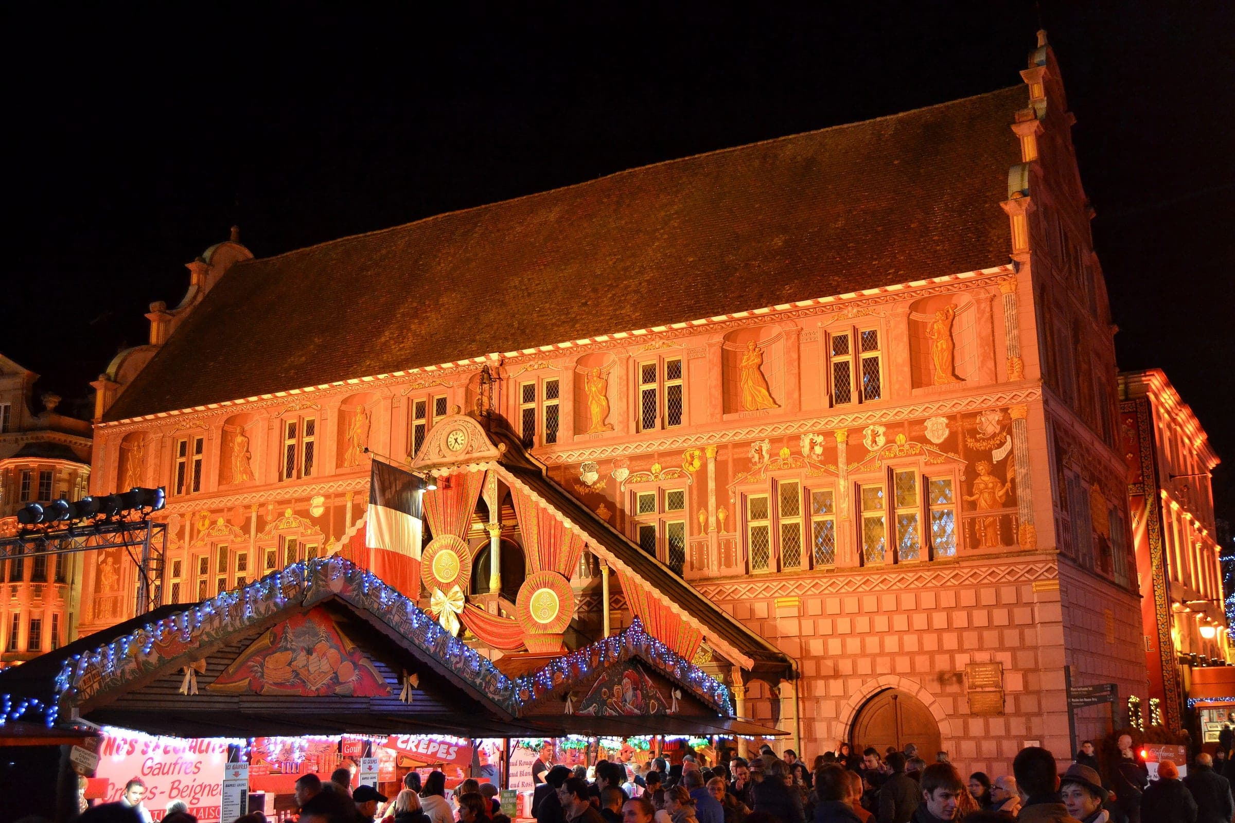 The painted Renaissance town hall of Mulhouse glows above the Christmas market chalets at night.