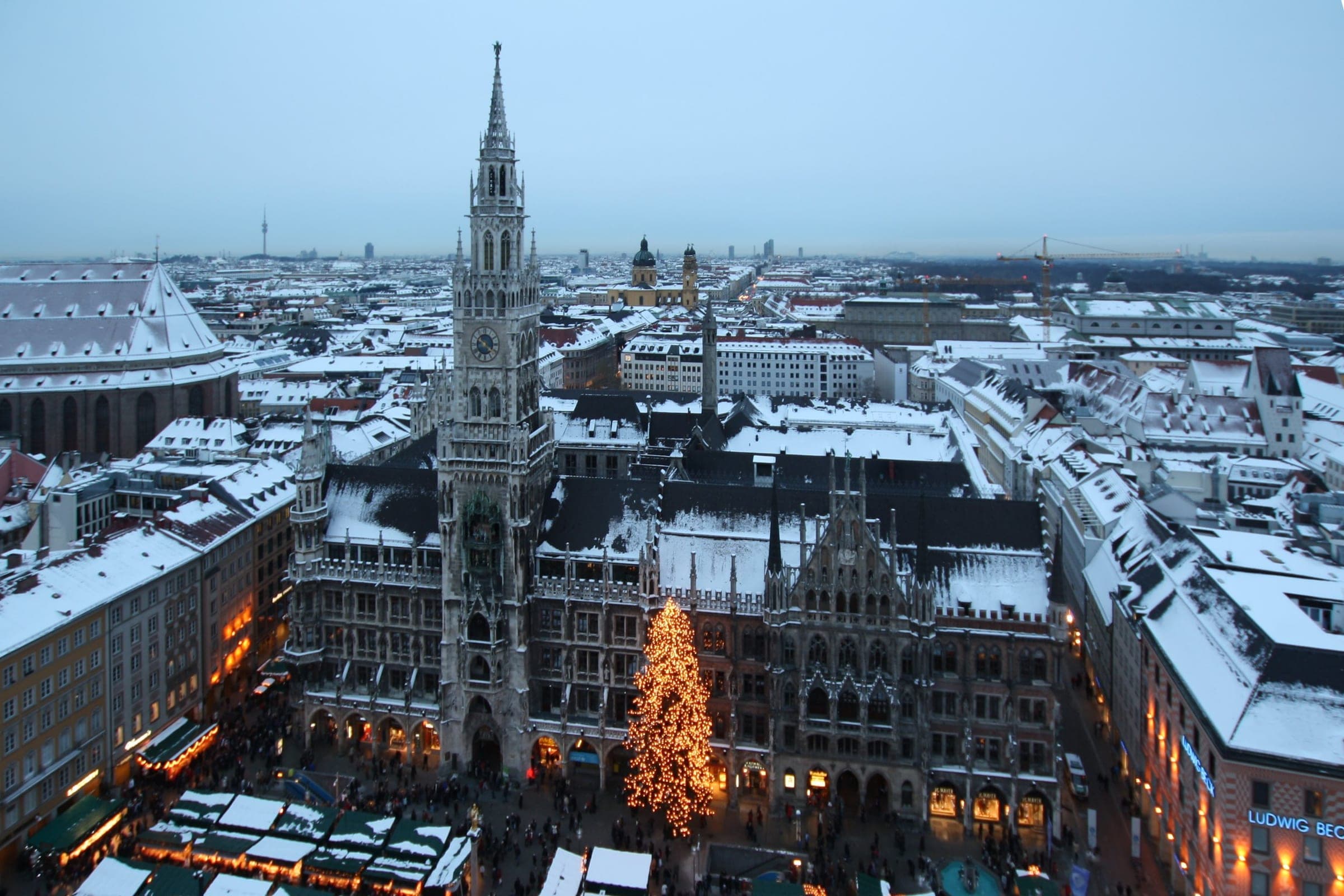 Snow covers the roofs around Marienplatz in Munich with the Neues Rathaus and the market tree below.