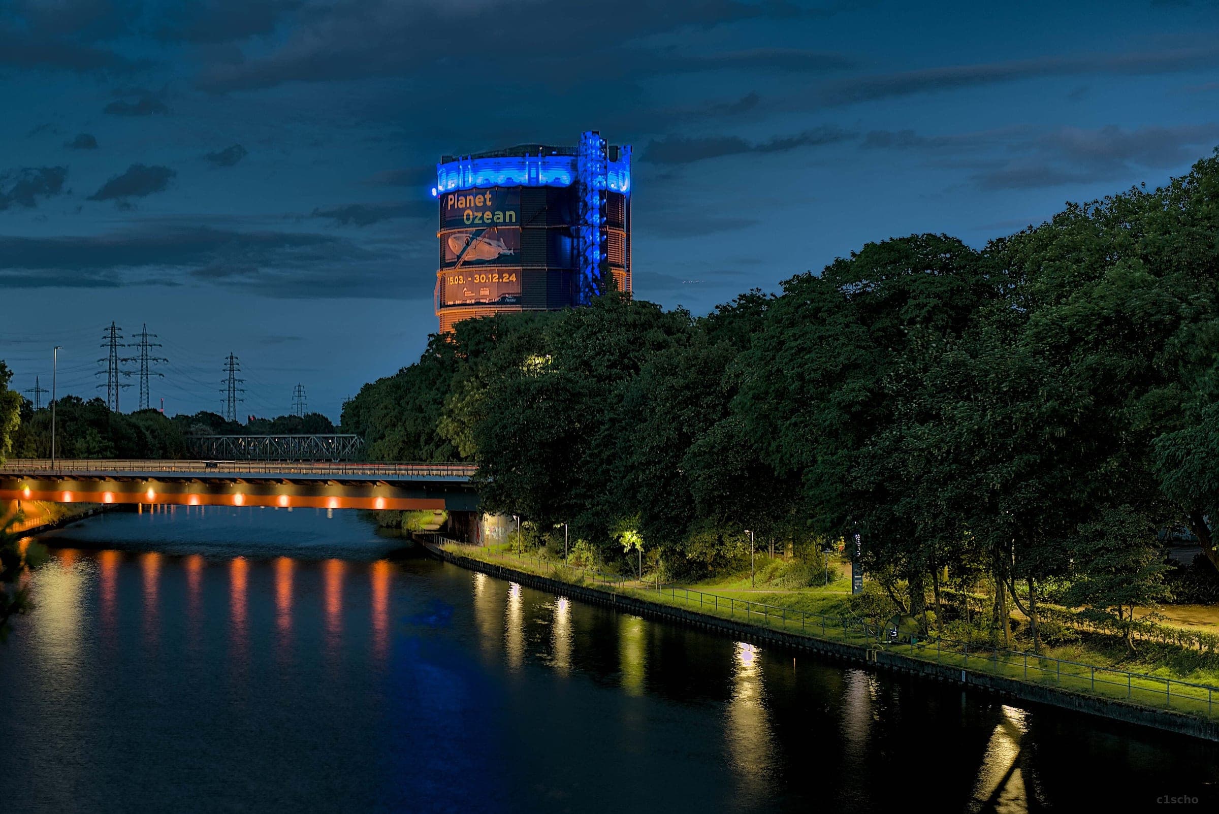 The Gasometer in Oberhausen glows blue at its crown above the Rhine-Herne Canal at blue hour
