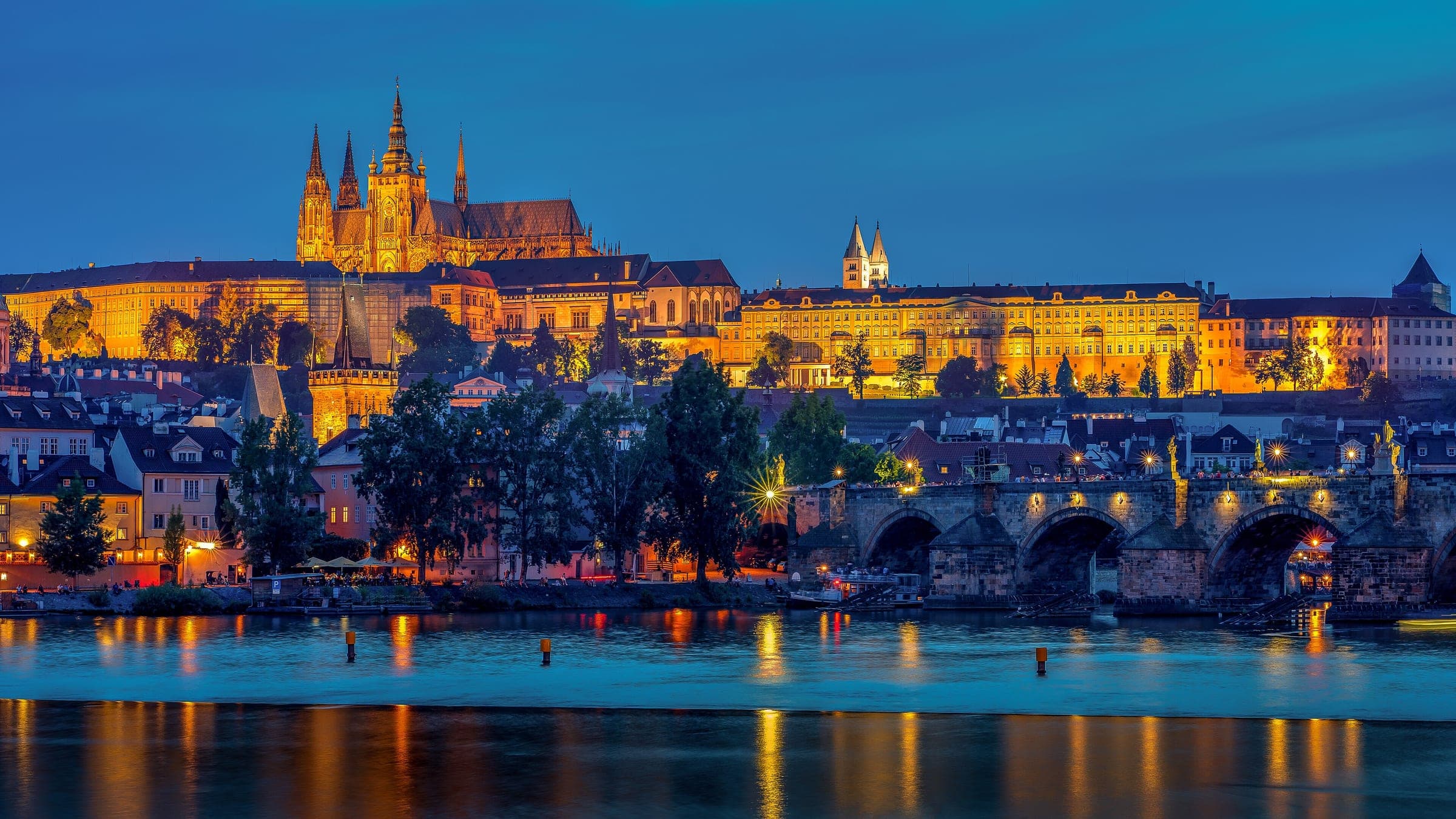 Prague Castle and St Vitus Cathedral light up at blue hour above Charles Bridge and the Vltava.