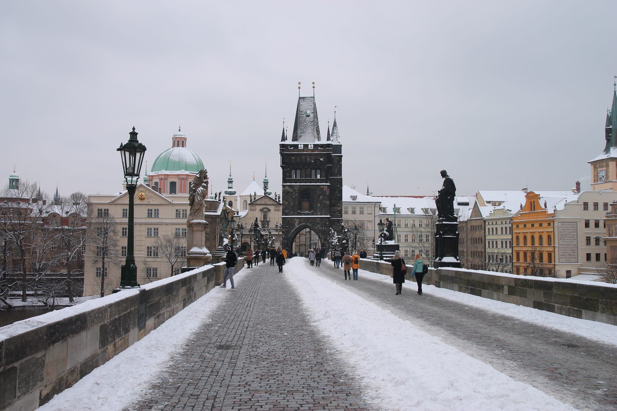 Fresh snow lies on Charles Bridge in Prague below the Old Town Bridge Tower and the bridge statues.