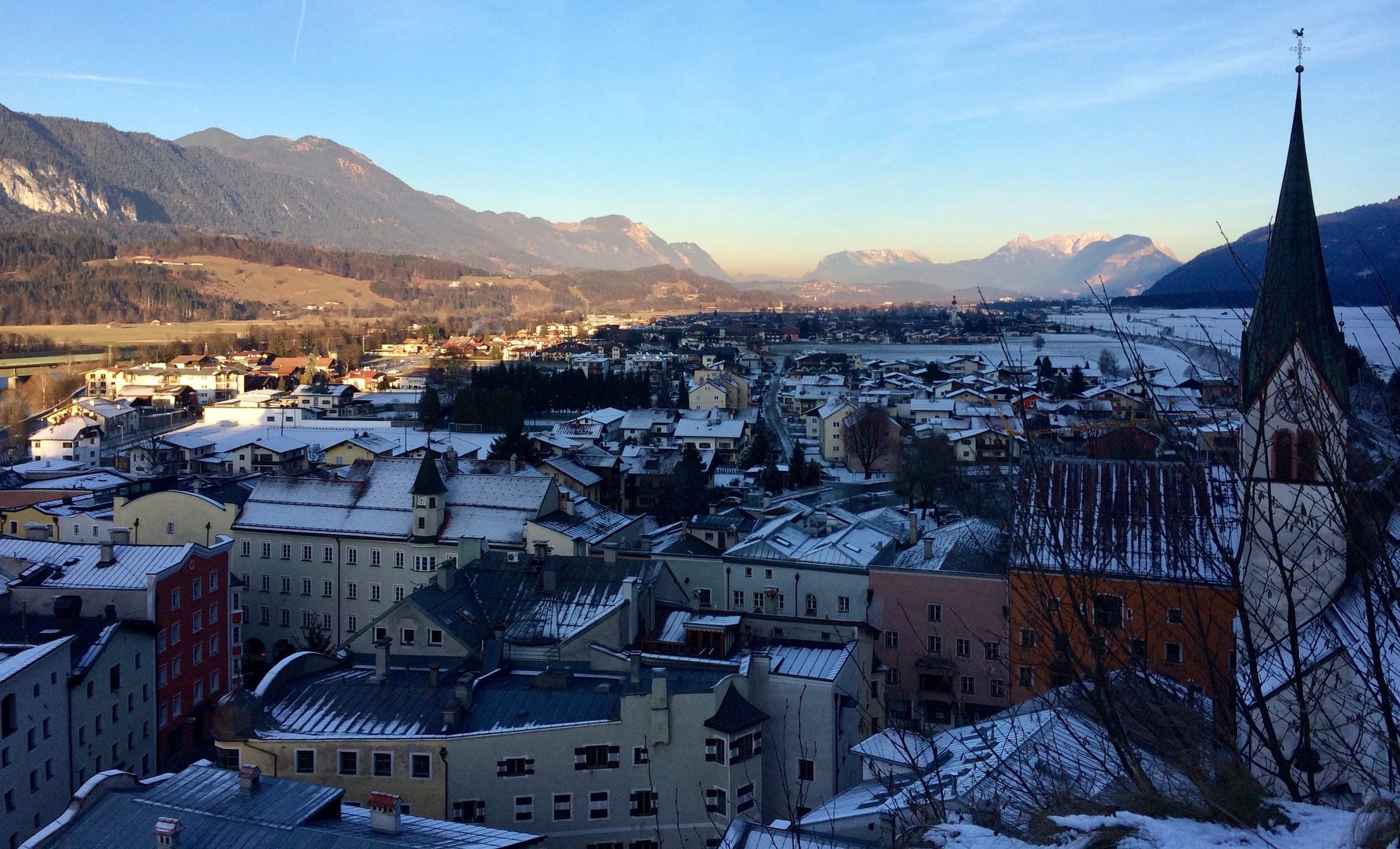 Snow dusts the rooftops of Rattenberg below its church spire, with the Inn valley stretching toward the Alps.