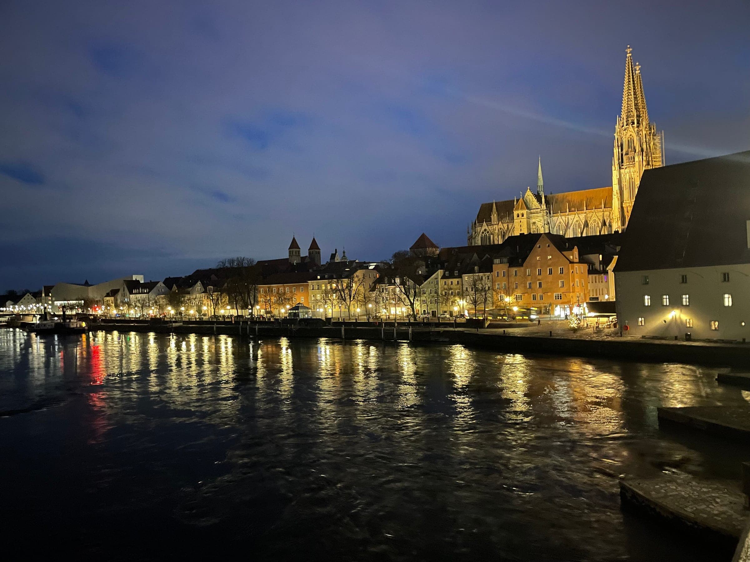 Regensburg's lit Danube waterfront and cathedral spires shine on a January night.