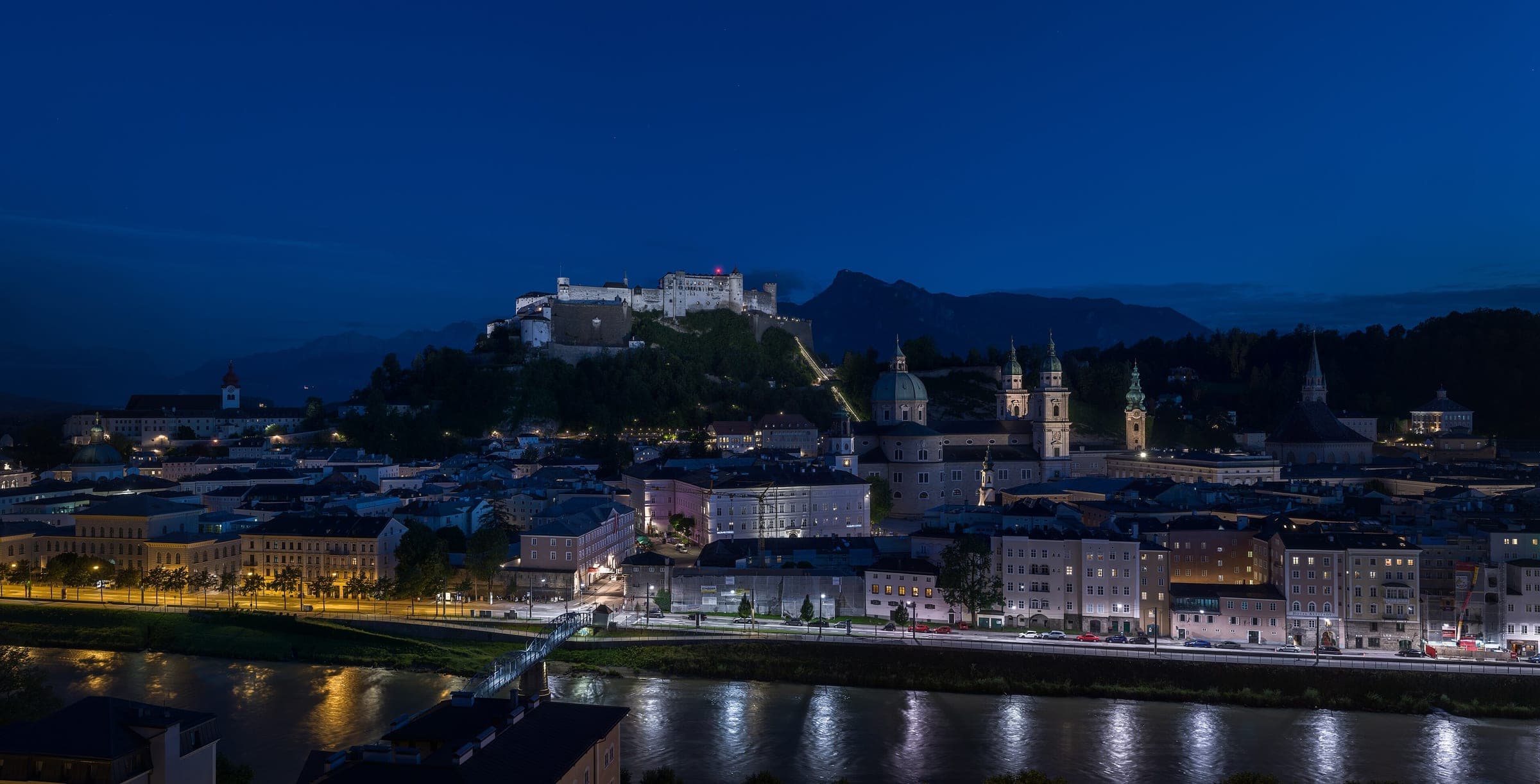 Hohensalzburg Fortress and the domes of Salzburg's old town glow above the Salzach at blue hour