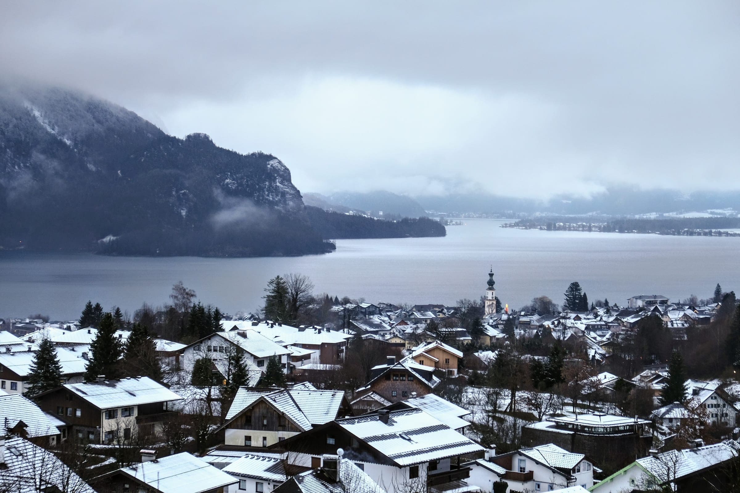 Snowy roofs of St Gilgen run down to the Wolfgangsee with the parish church spire at the centre