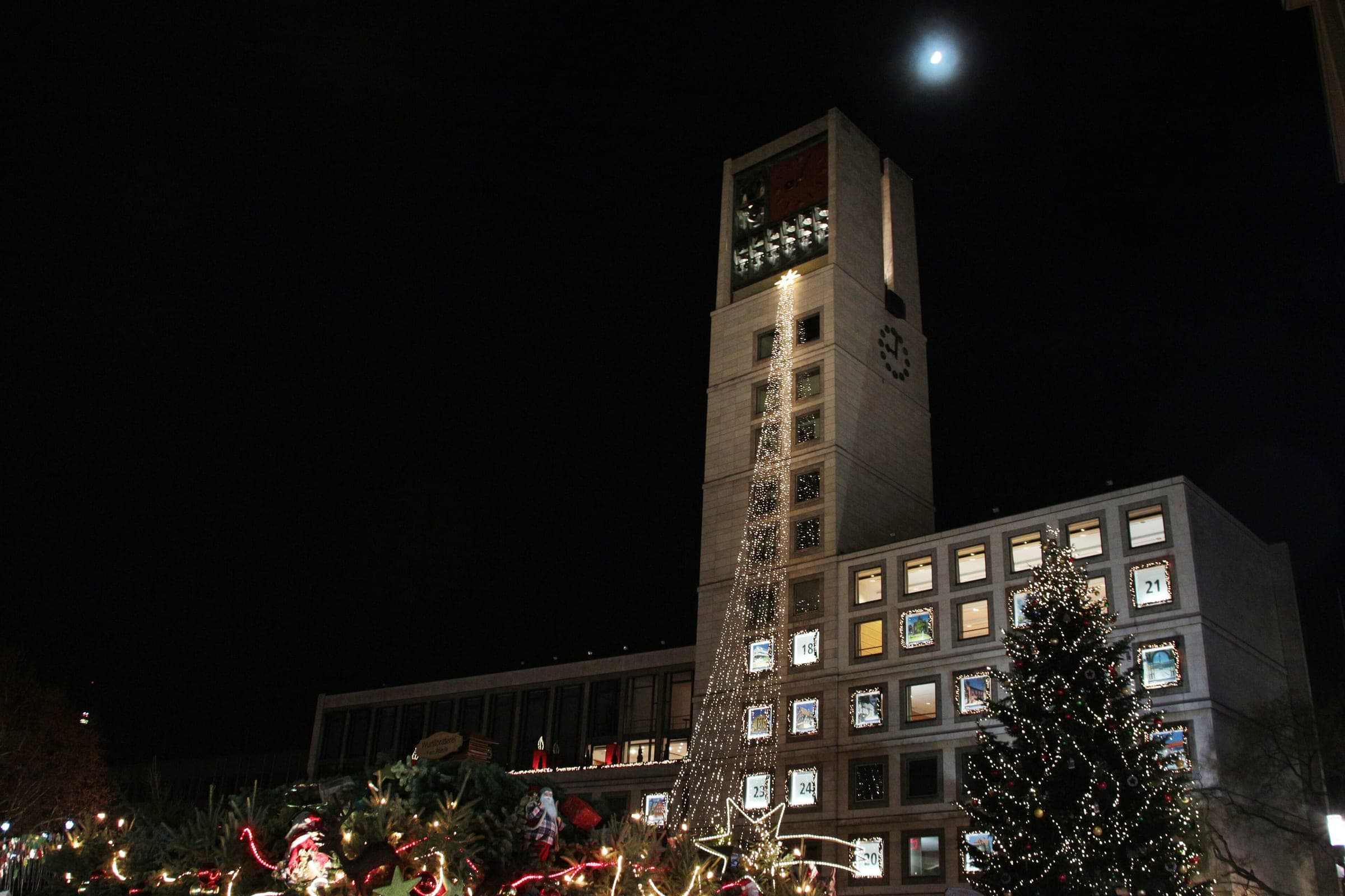 Stuttgart's Rathaus tower rises over the lit Marktplatz stalls and Christmas tree on a December night.