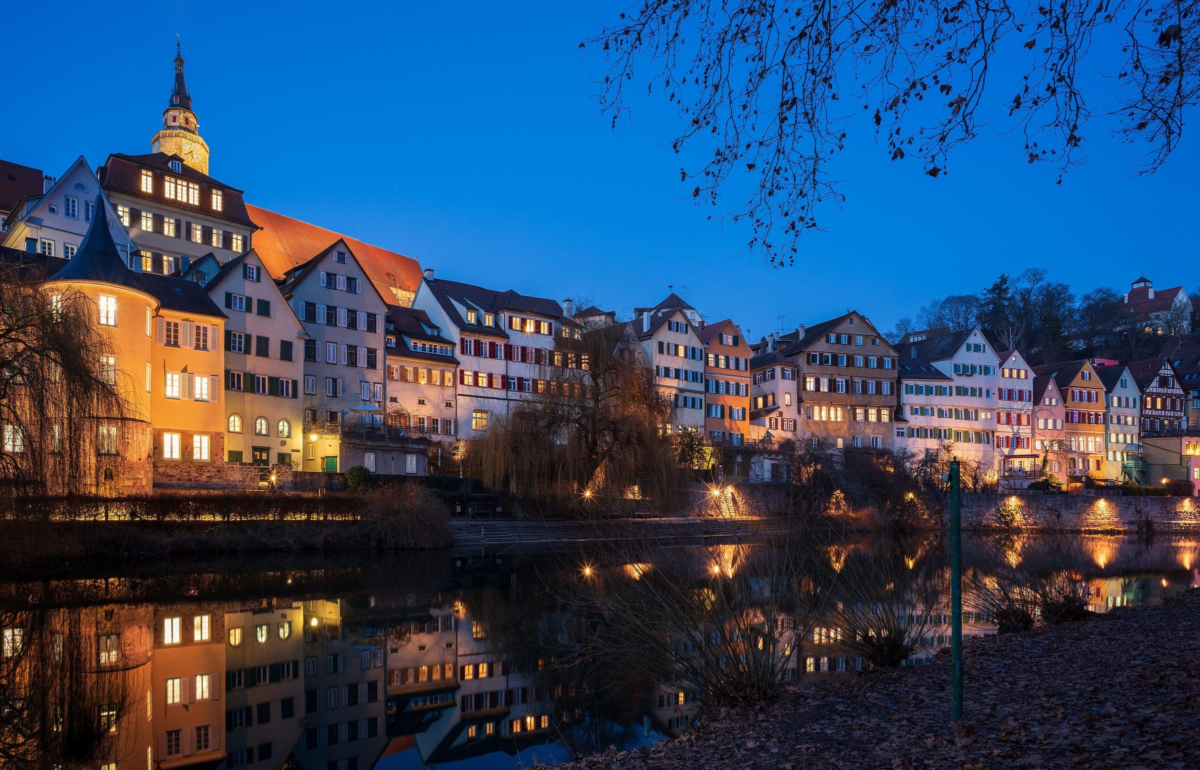 Lit windows of Tübingen's Neckarfront and the Hölderlinturm shine on the still river at blue hour.