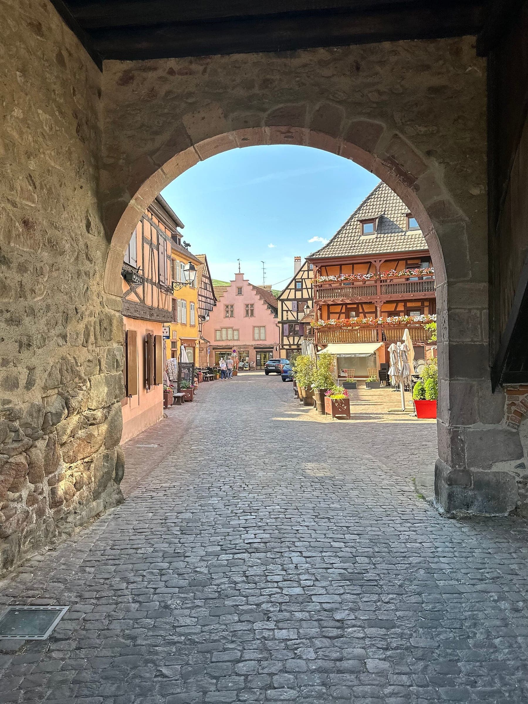 An old stone arch in Turckheim frames a cobbled square lined with painted half-timbered houses.