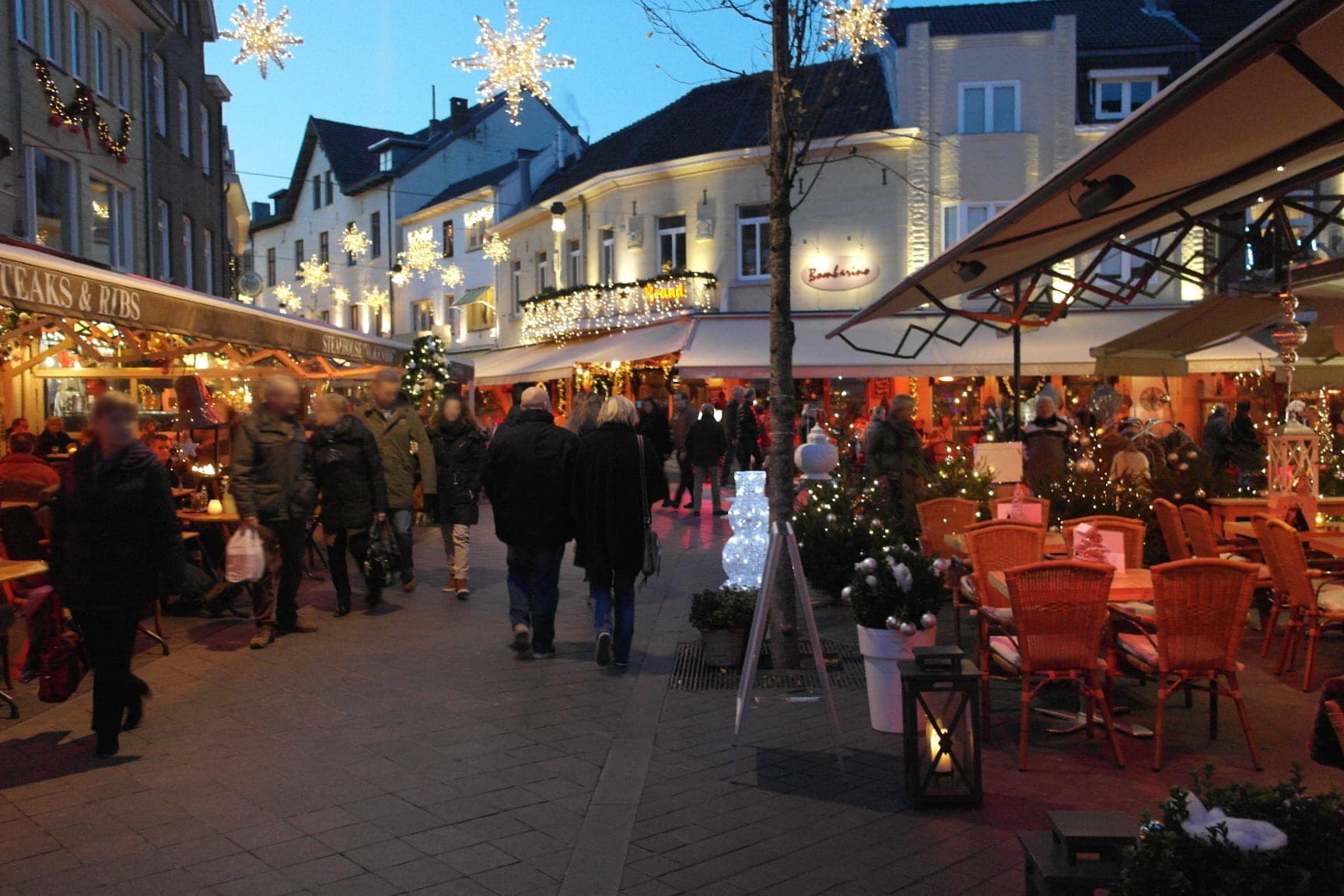 Strollers pass café terraces under star lights on Berkelstraat in Valkenburg at dusk.