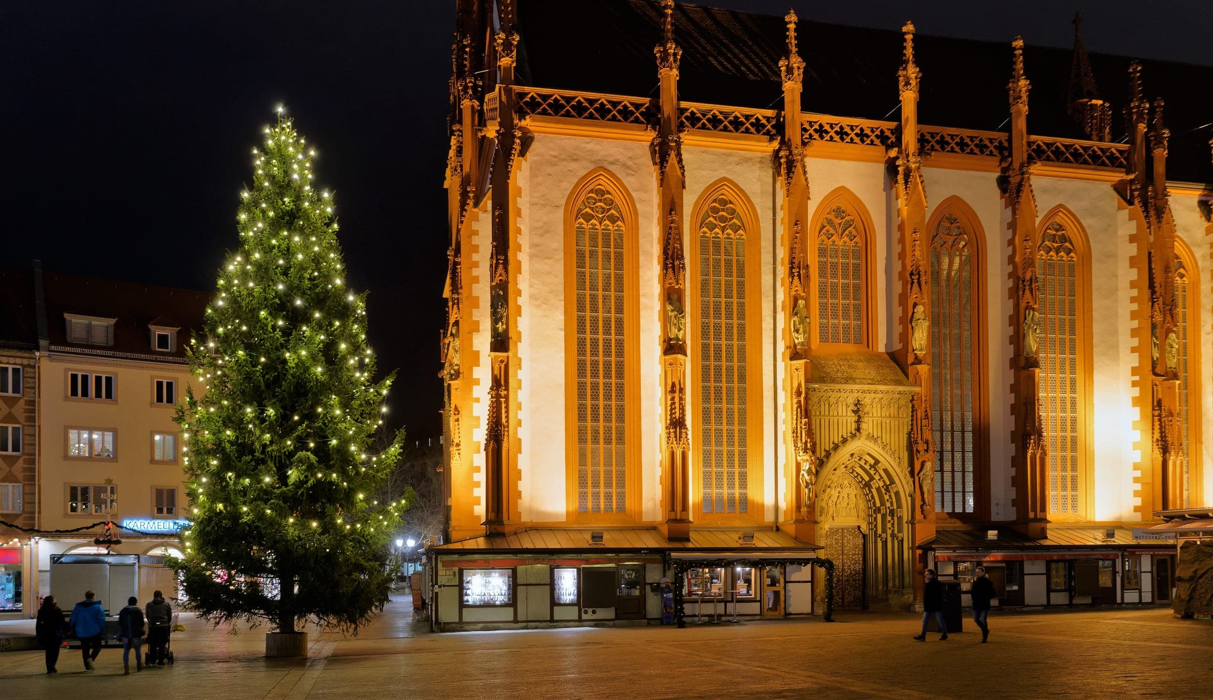 A lit Christmas tree stands beside the floodlit Marienkapelle on Würzburg's Marktplatz at night