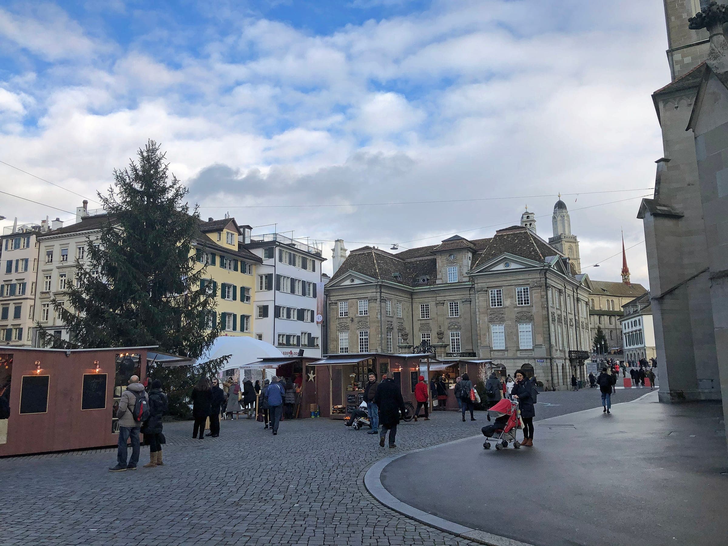 A tall Christmas tree and market huts stand on the Münsterhof in Zurich beside the Fraumünster