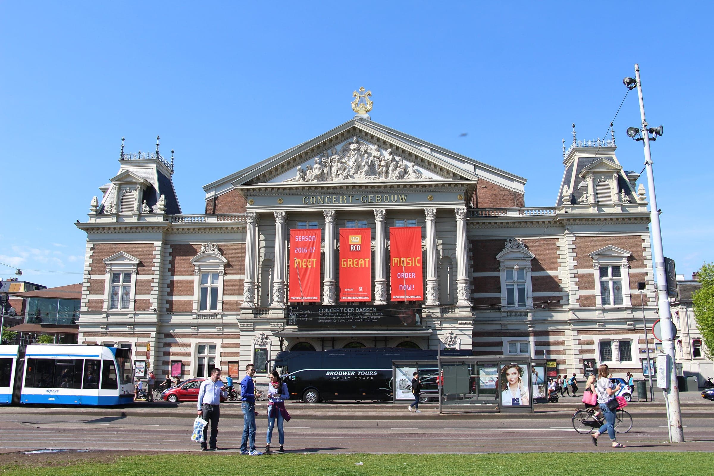 A tram stands at the stop beside the columned brick facade of the Concertgebouw in Amsterdam.