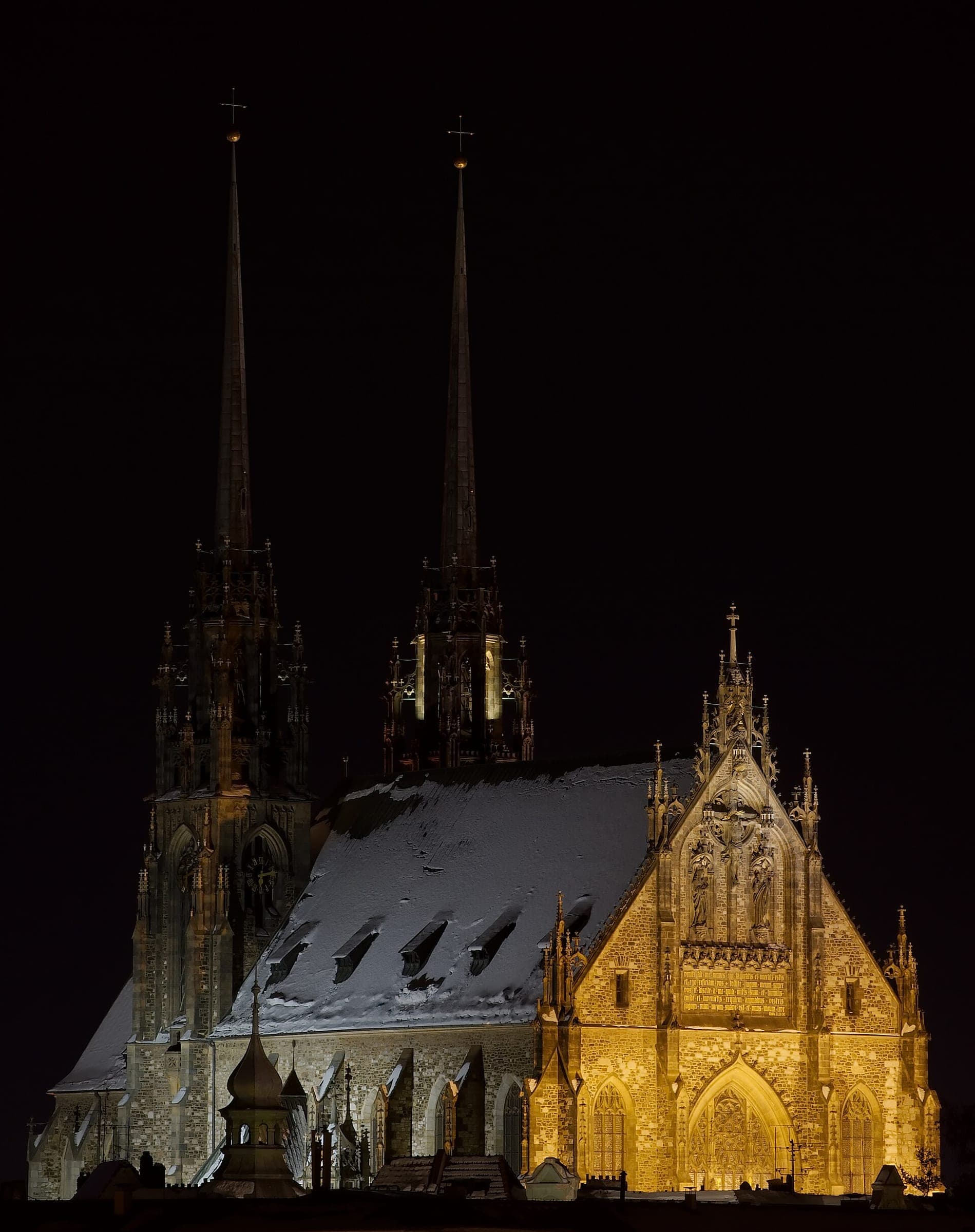 Snow covers the roof of the Cathedral of Saints Peter and Paul in Brno as floodlights catch its spires at night.