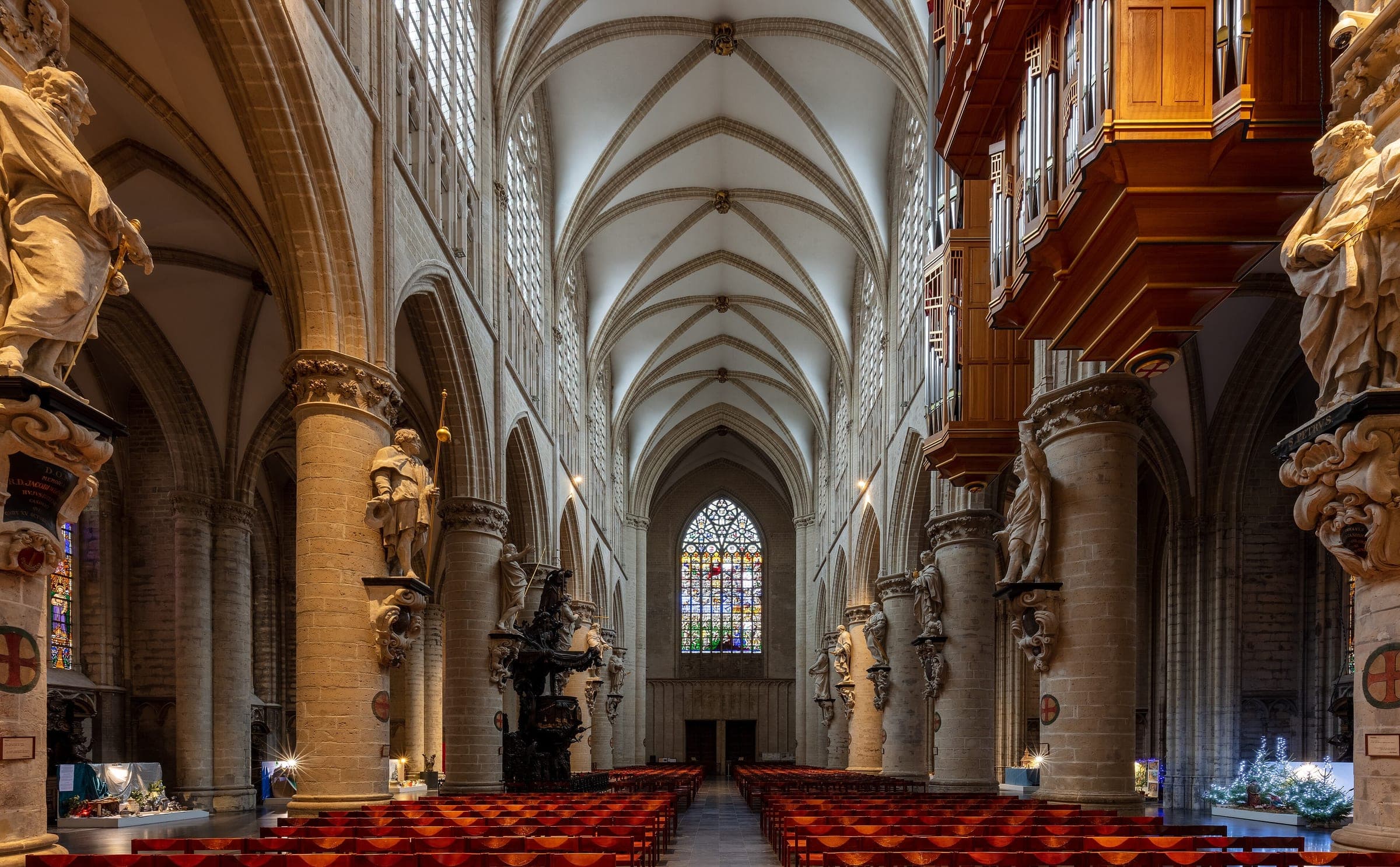Baroque statues line the pillars of the white Gothic nave of the Brussels cathedral beside its organ.