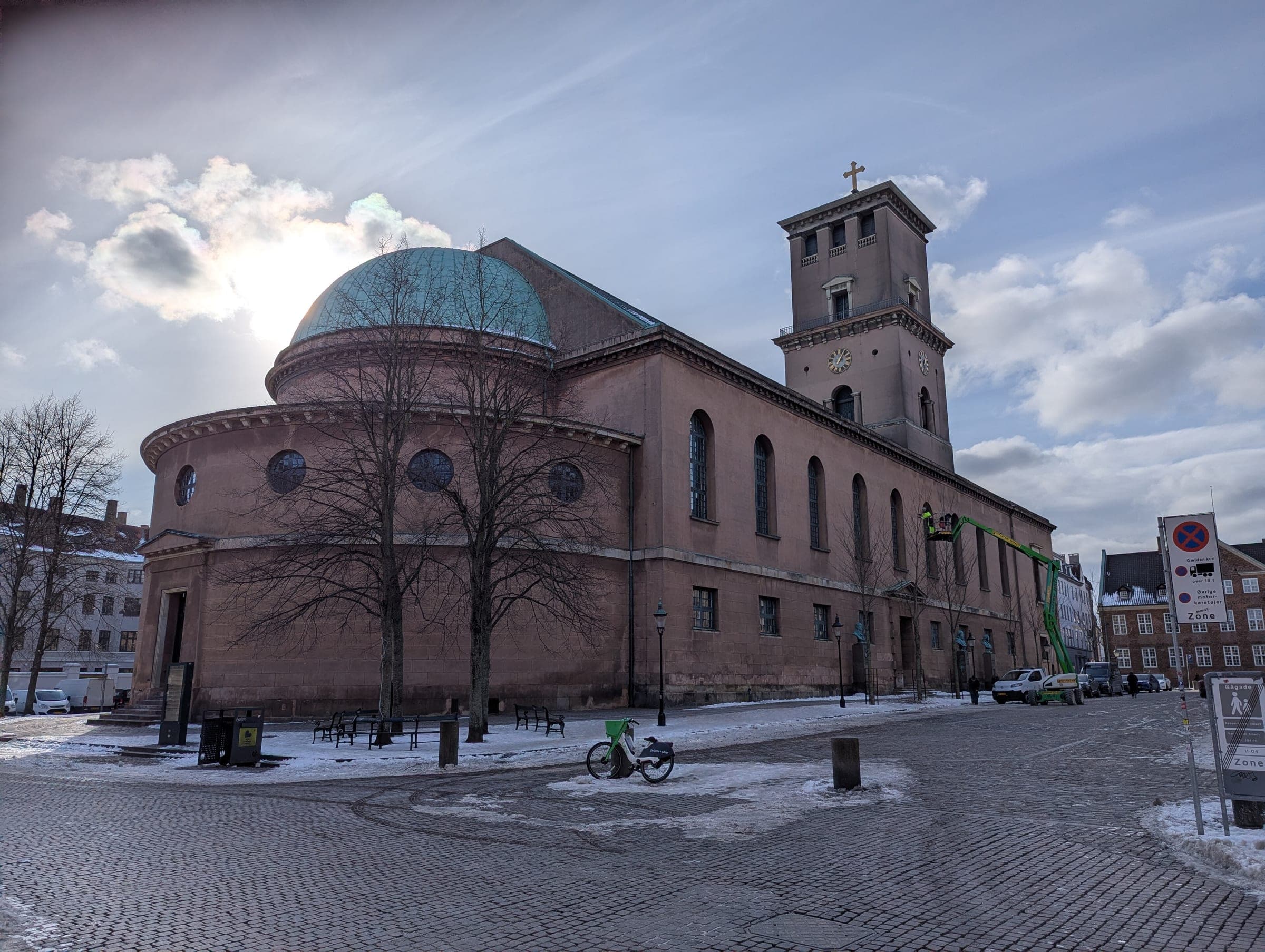 Snow lies on the paving around the domed apse and tower of Copenhagen Cathedral on a winter afternoon.