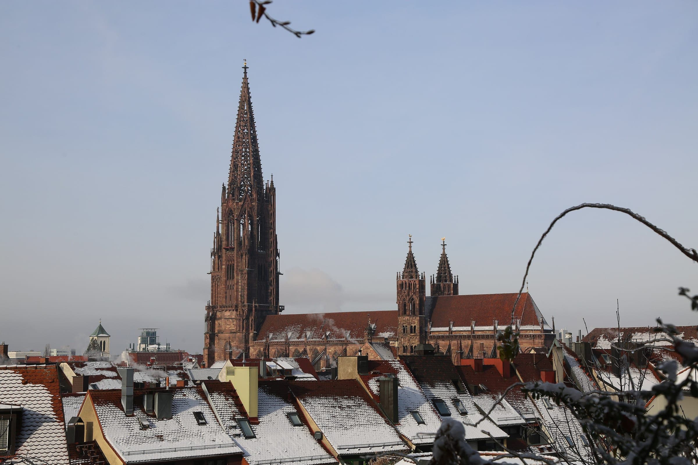 The spire of Freiburg Minster rises above snowy old town roofs seen from the Schlossberg.