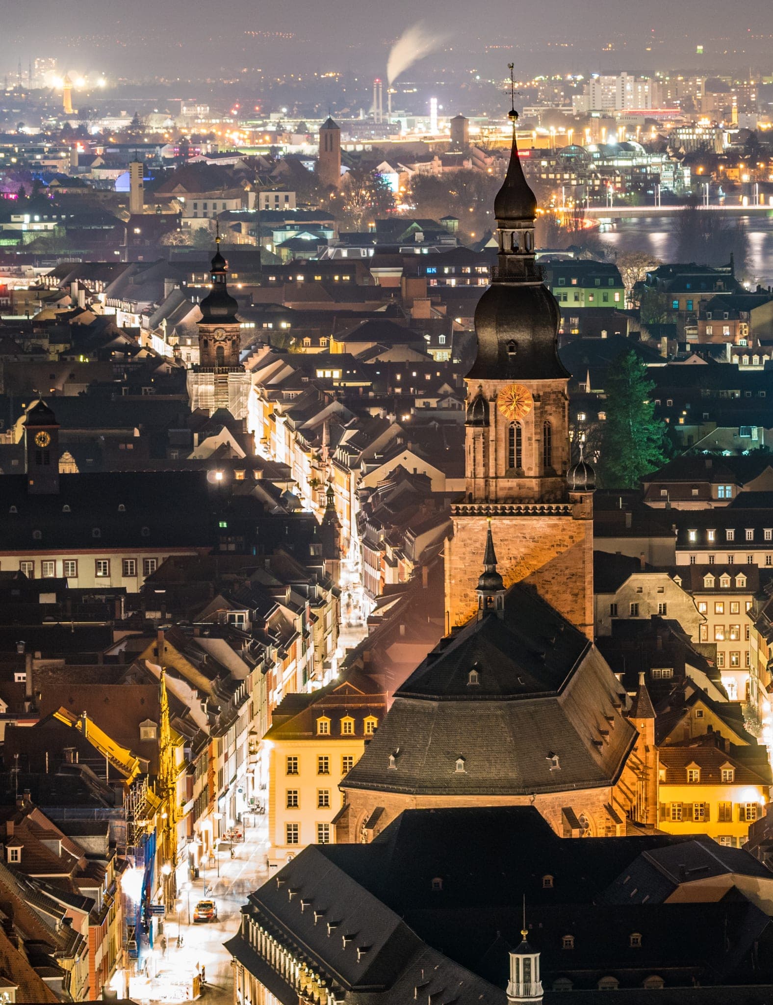 The tower of the Heiliggeistkirche rises above the lit lanes of Heidelberg's old town at night.