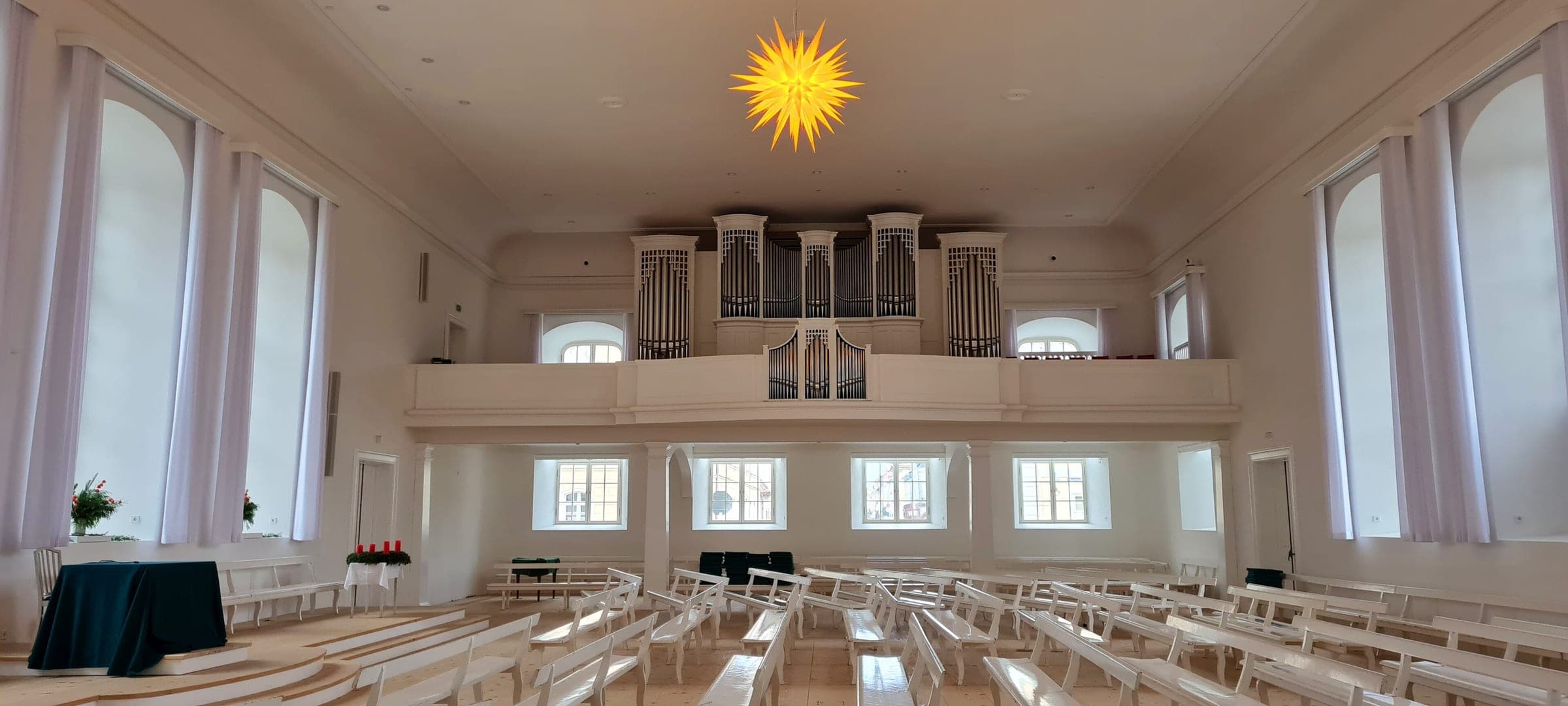 White benches face the organ gallery in the plain white Kirchensaal of the Moravian Church in Herrnhut.