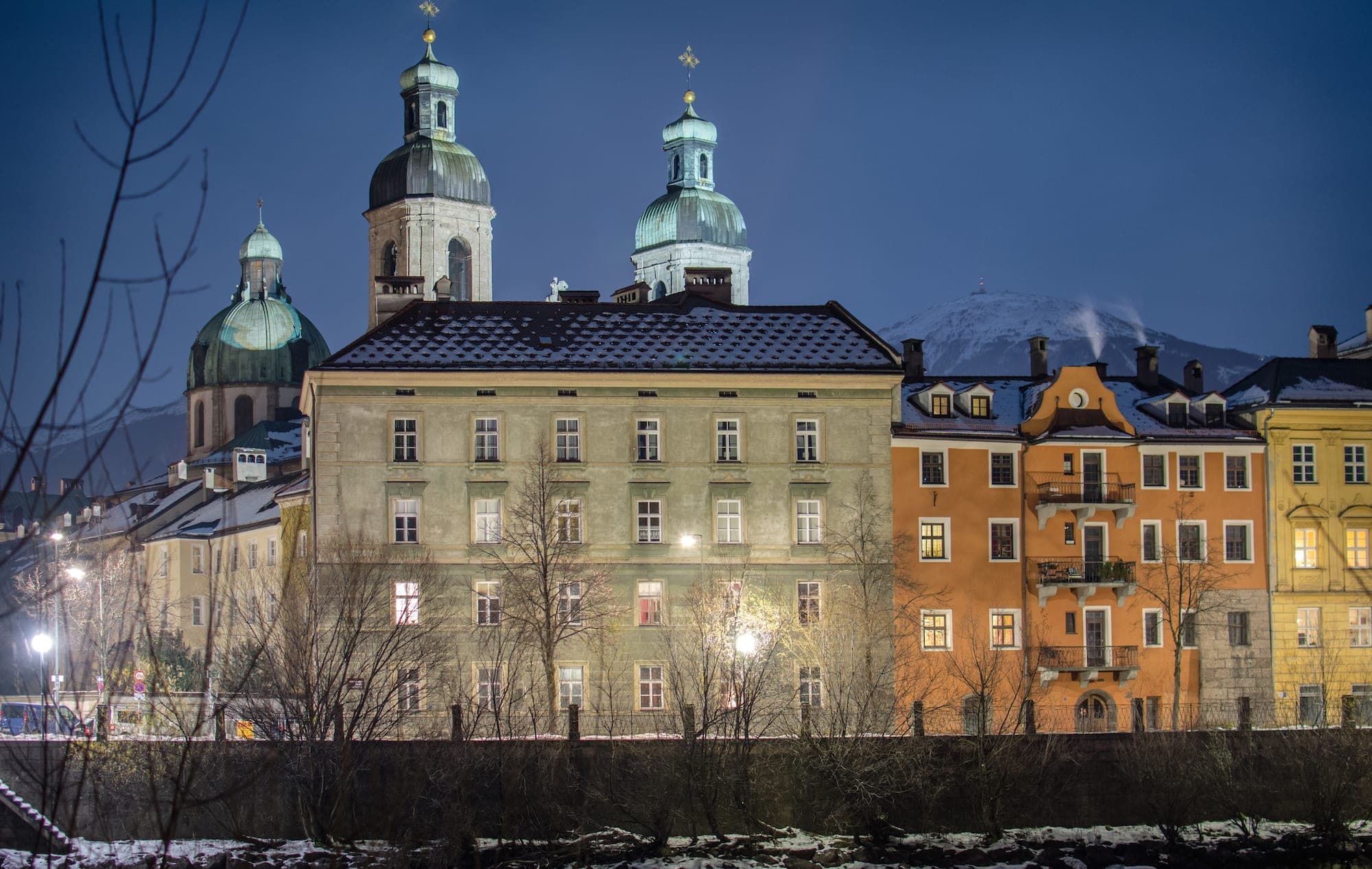 The twin towers and dome of Innsbruck Cathedral rise behind the Hofburg roofs at blue hour in January.