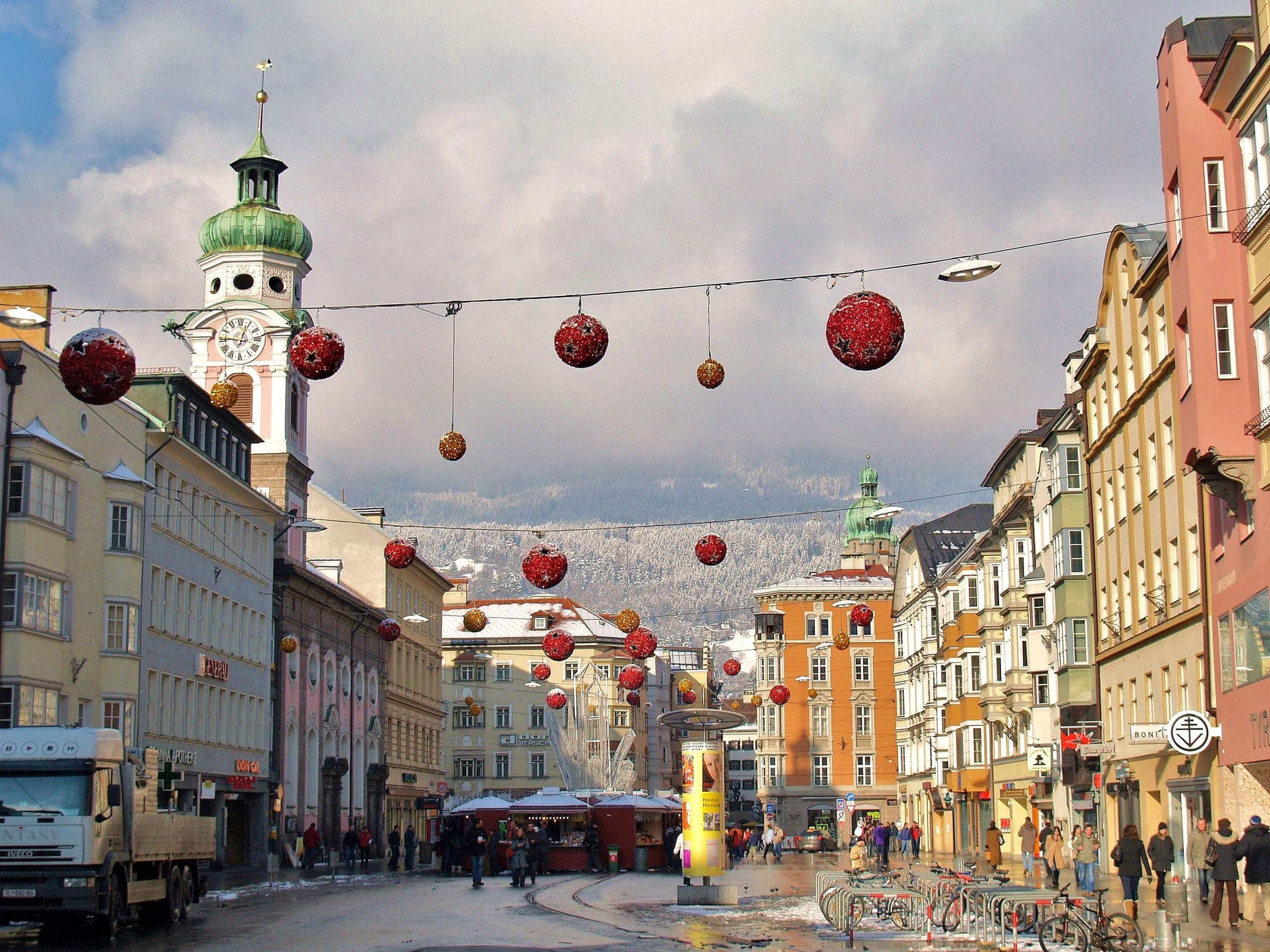 Red Christmas baubles hang over Maria-Theresien-Straße in Innsbruck, with the Spitalskirche tower on the left.
