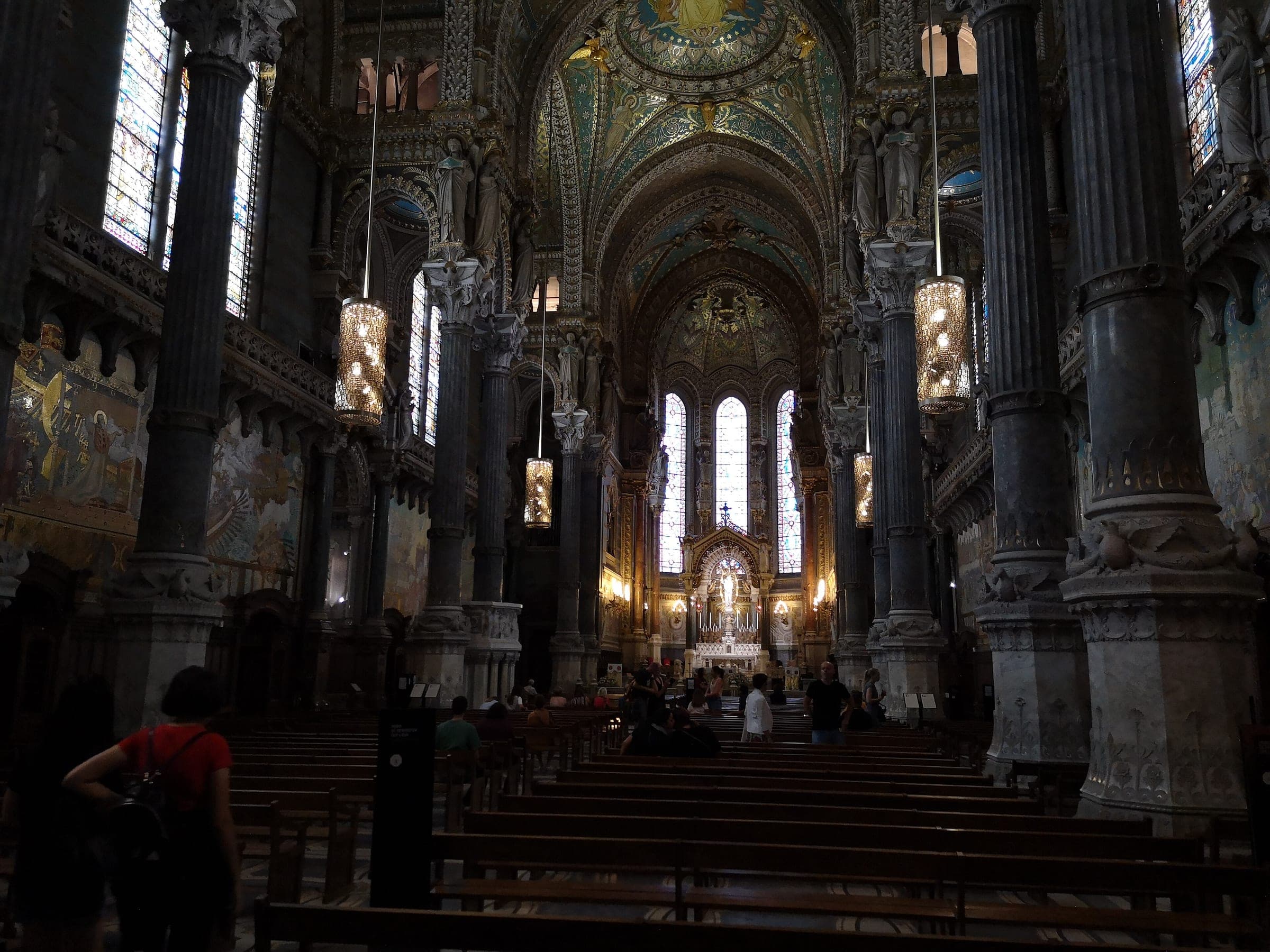 Hanging lanterns light the dark marble columns of the Fourvière basilica nave toward its high altar in Lyon.