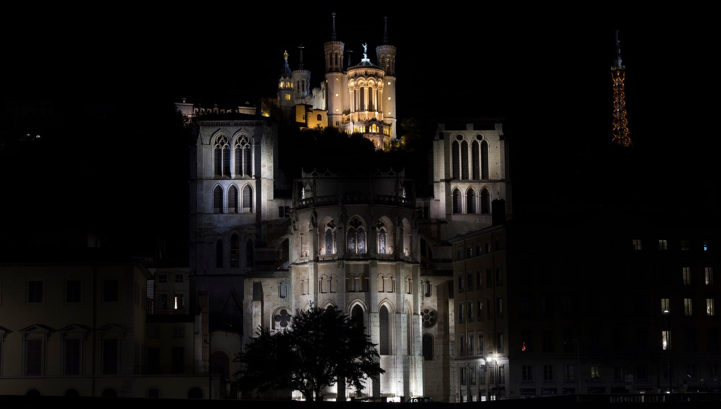 The apse of Saint-Jean Cathedral glows below the lit Fourvière basilica on its hill in Lyon at night.