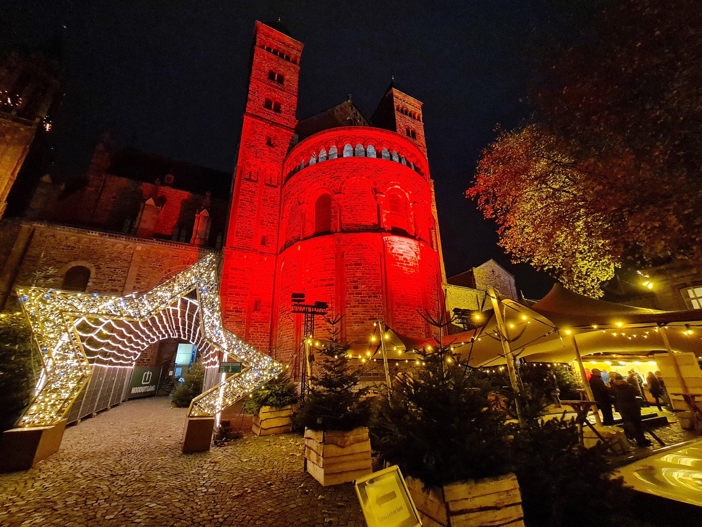 Red light floods the Basilica of Saint Servatius in Maastricht above a lit arch and the Vrijthof Christmas stalls.
