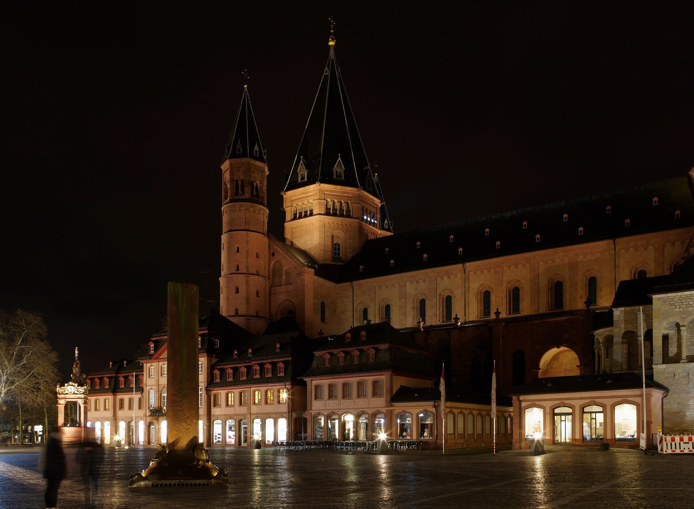 Mainz Cathedral's towers rise behind the lit houses of the empty Markt on a damp night.