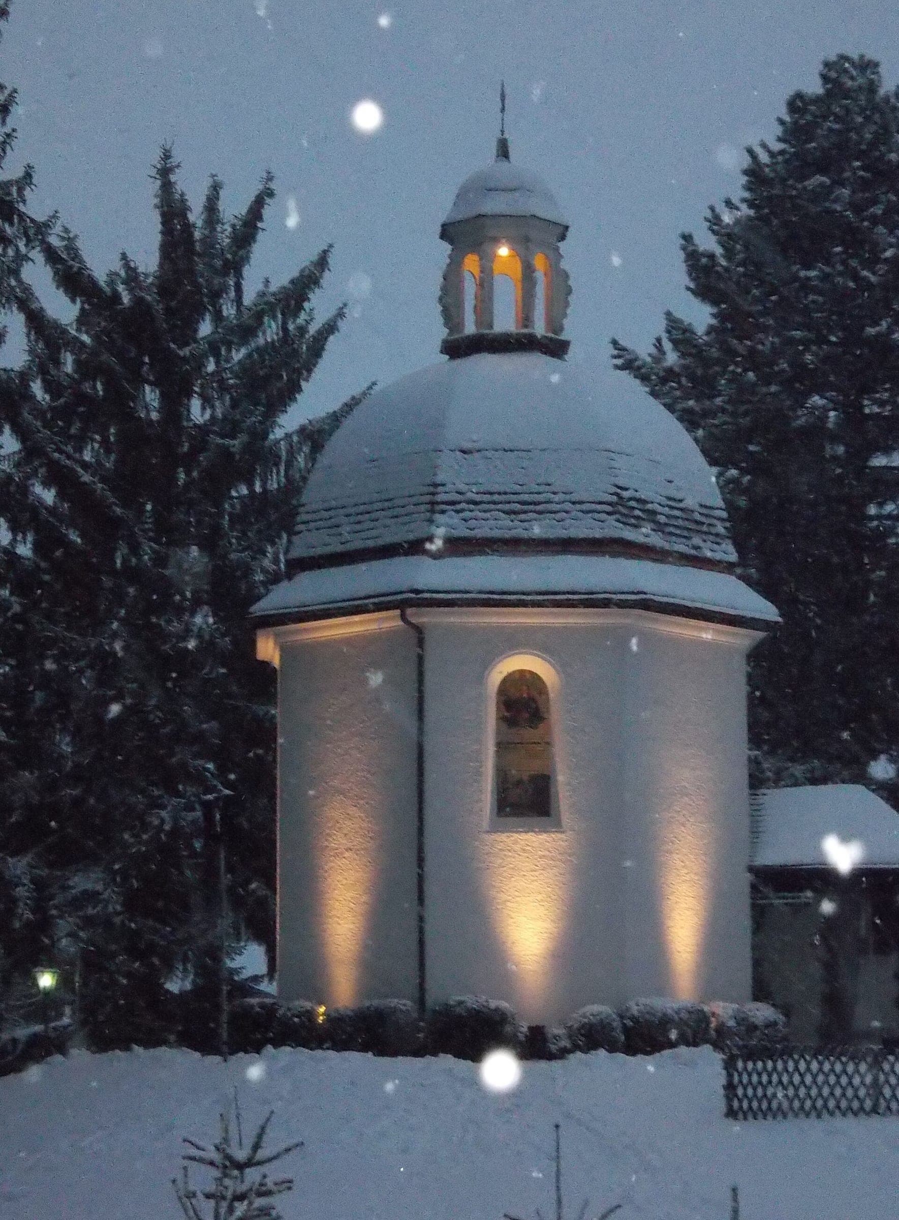 Snow falls past the floodlit Silent Night Chapel in Oberndorf at nightfall