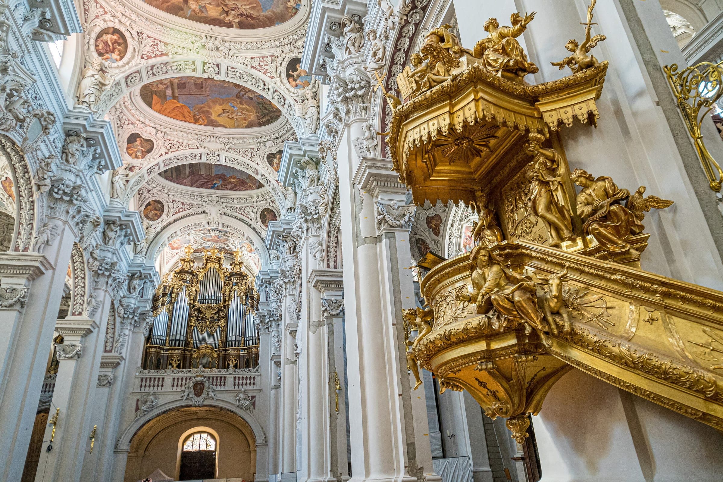 The gilded pulpit and the great organ fill the white Baroque nave of St. Stephen's Cathedral in Passau.