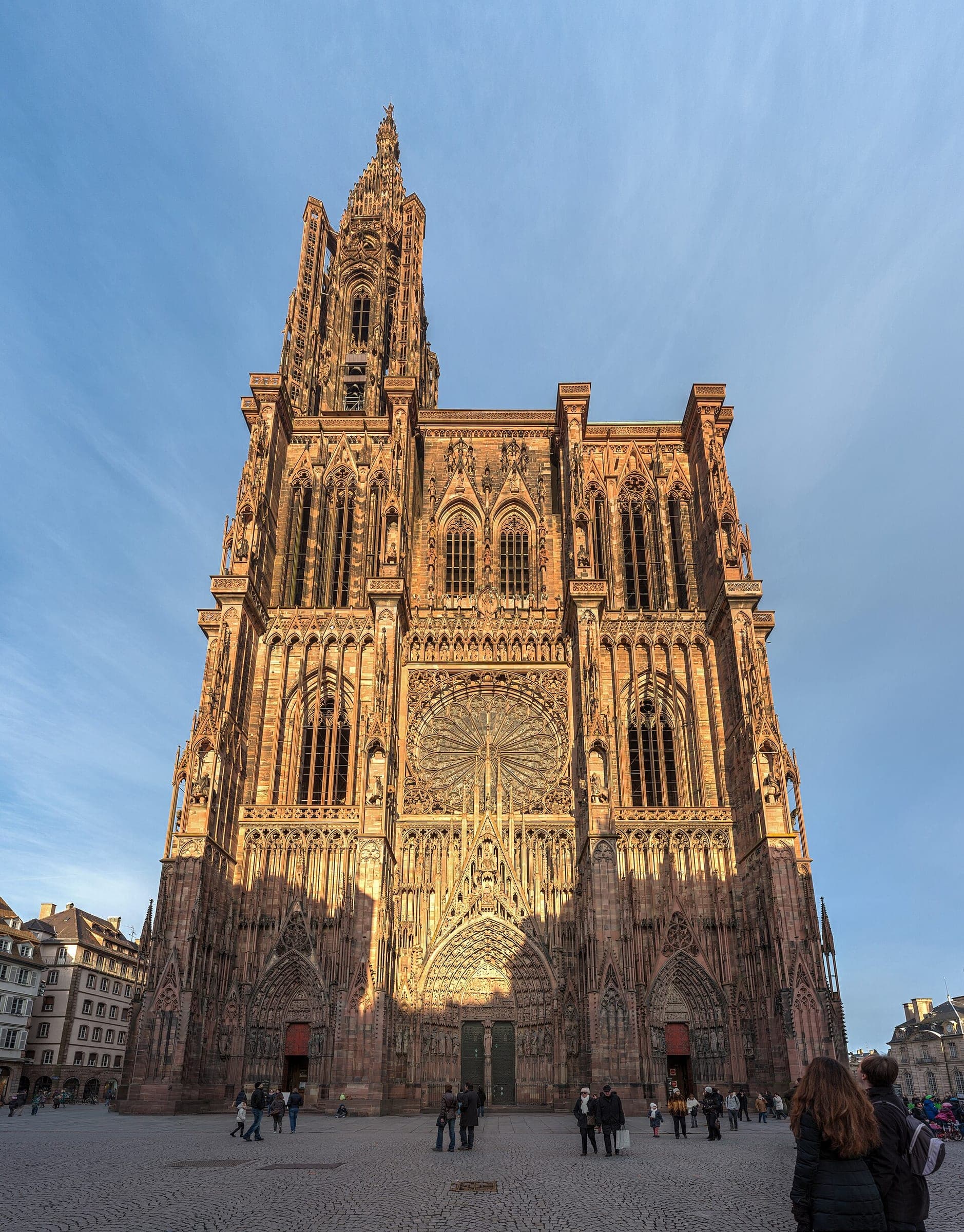 Low sun warms the pink sandstone west front and single spire of Strasbourg Cathedral.