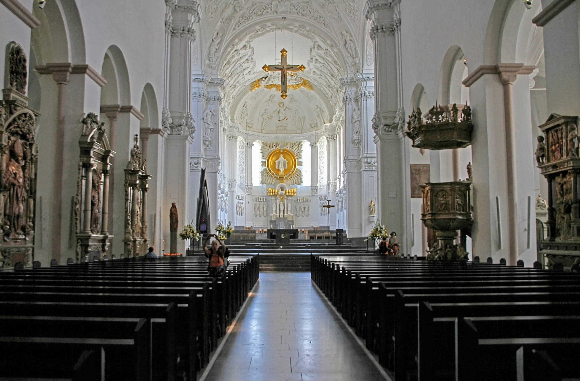 White stucco vaults and a gilded cross hang over the long nave of Würzburg Cathedral toward the choir