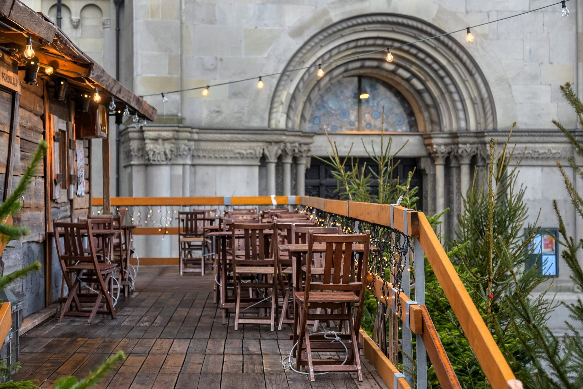 A wooden market terrace with fairy lights stands beside the Romanesque north portal of the Grossmünster in Zurich